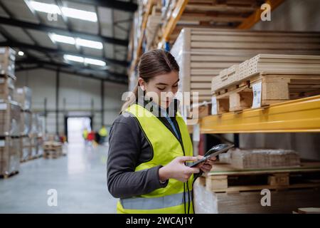 Female warehouse worker holding scanner, scanning the barcodes on products in warehouse. Warehouse manager using warehouse scanning system. Stock Photo