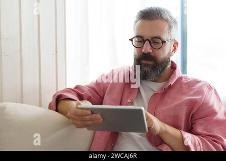 Man using smart thermostat, adjusting, lowering heating temperature at home. Man watching tv show on tablet, video streaming services with movies and Stock Photo