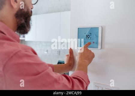 Man using smart thermostat, adjusting, lowering heating temperature at home. Concept of sustainable, efficient, and smart technology in home heating Stock Photo