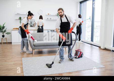 Portrait of professional bearded cleaner from cleaning service vacuums carpet. Stock Photo