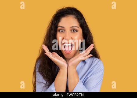 Joyful young woman with curly hair, hands framing her face, mouth open in a playful shout Stock Photo