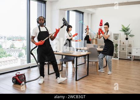 African man with modern vacuum cleaner and three cleaners dancing. Stock Photo