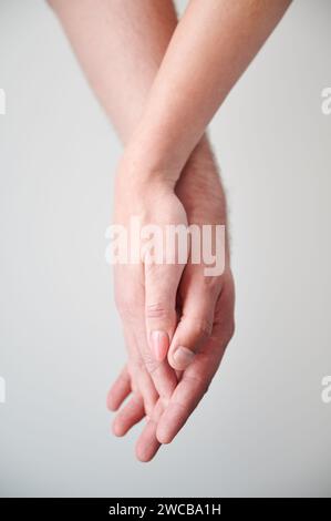 Close up view of hands of sweet couple. Young man and woman holding hands on light neutral background. Concept of love, intimacy, support, and trust. Stock Photo