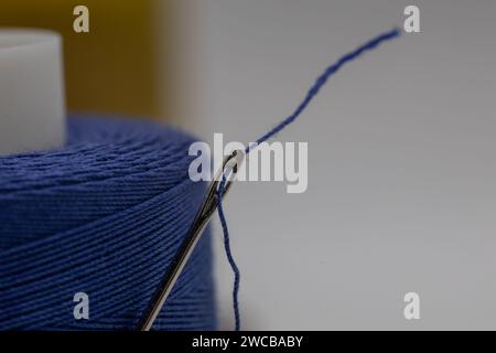 A closeup of a small needle in a blue thread on the blurry background Stock Photo