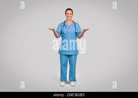 Smiling female doctor wearing blue medical uniform coat and stethoscope talking to camera, explaining and gesturing Stock Photo