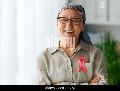 Female patient standing near window and smiling. Raising knowledge on people living with tumor illness. Stock Photo