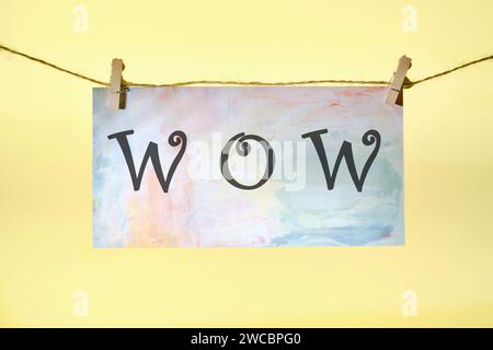 WOW lettering on colored paper hanging in front of a yellow background with a rope and clothespins Stock Photo