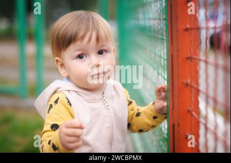In a world of boundless wonder, a little boy discovers magic and curiosity while standing next to a striking red fence Stock Photo