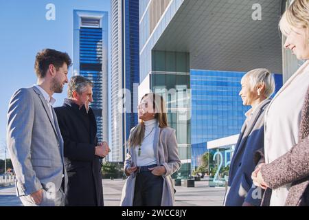 Group of coworkers outside in front of office buildings discuss about business plan. Stock Photo