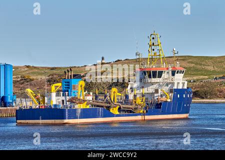 Dredger vessel in marine port during sunny day with mountain on the background. Stock Photo