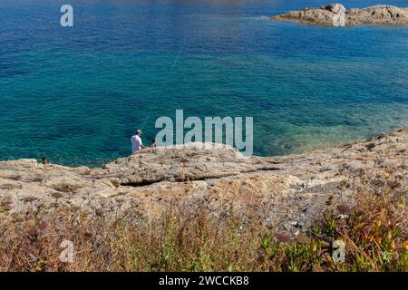 Ile Rousse, Corsica, 2017. Holidaymakers fishing in the crystal clear sea off the rocky promontory of the Ile de la Pietra Stock Photo