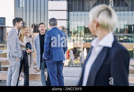 group of businessmen laughing and chatting while a woman in the foreground, out of focus, looks at them. Stock Photo