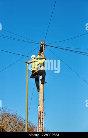 A telephone engineer fixing cabling on the top of a telegraph pole Stock Photo