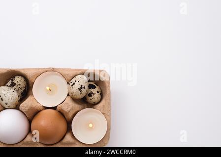 Eggs and candle in eggshell in tray on white background. Quail and chicken eggs. Copy space. Easter holiday concept Stock Photo