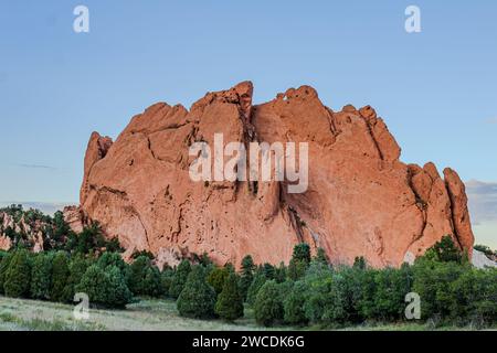 Early morning light on a dramatic red sandstone rock formation surrounded by greenery Stock Photo
