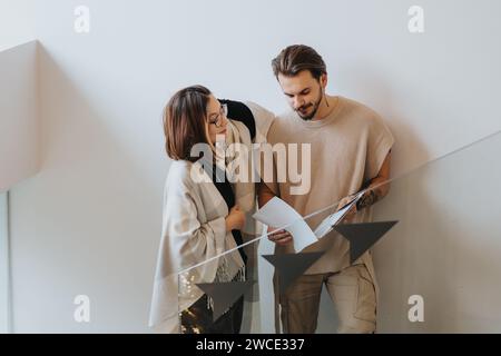 Focused professionals standing on stairs collaborating and analyzing project solutions in a modern office. Stock Photo
