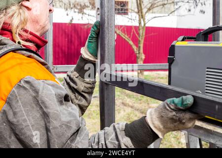 A man installs an iron frame for construction. Welding metal profiles. Stock Photo