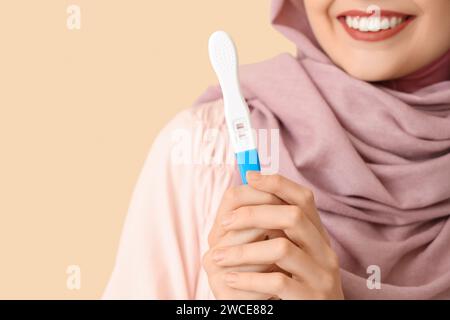 Happy Muslim woman with positive pregnancy test on beige background Stock Photo