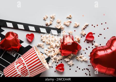 Movie clapper with bucket of popcorn and heart shaped decor on white background. Valentine's Day celebration Stock Photo