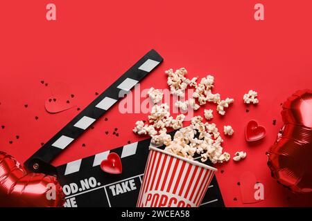 Movie clapper with bucket of popcorn and heart shaped decor on red background. Valentine's Day celebration Stock Photo