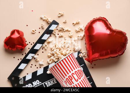 Bucket of popcorn with movie clapper and heart shaped balloons on beige background. Valentine's Day celebration Stock Photo