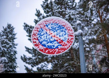 A road sign prohibiting parking is covered with sticky snow. 'No Parking' sign under the snow shot close-up. Stock Photo