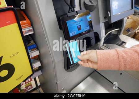 Hispanic woman slides a credit card into a reader while using self-checkout at a Kroger grocery store in Bedford, TX  - November 2023 Stock Photo