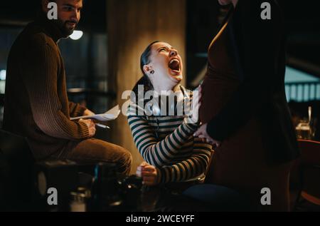 A beautiful, happy, businesswoman touches the stomach of her pregnant cousin and laughs after feeling the baby's kick. Stock Photo
