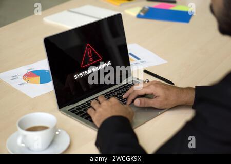 Back view of businessman in suit sit at desk in office, looks worried while using laptop computer which displays a red warning sign on the screen. Stock Photo