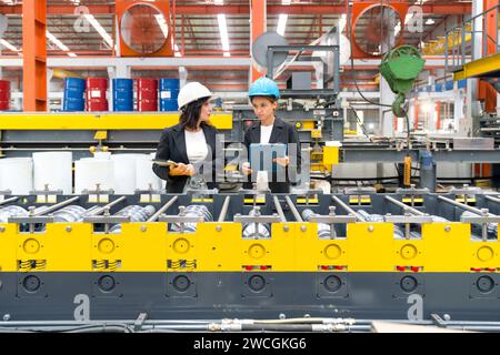 Two women operate machinery in a factory, wearing safety gear and focused on their task. Stock Photo