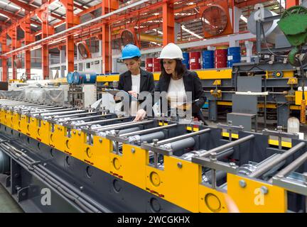 Two women operate machinery in a factory, wearing safety gear and focused on their task. Stock Photo