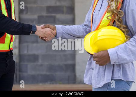 Two individuals shaking hands in front of a construction site as a gesture of agreement and partnership. Stock Photo