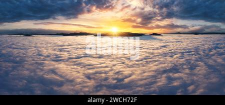 Beautiful sunset sky above the clouds with silhouettes of mountain peaks with dramatic light. Aerial drine view. Stock Photo