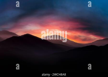 Mountain landscape at sunrise. Dramatic cloudy sunrise sky over mountain tops in morning fog Stock Photo