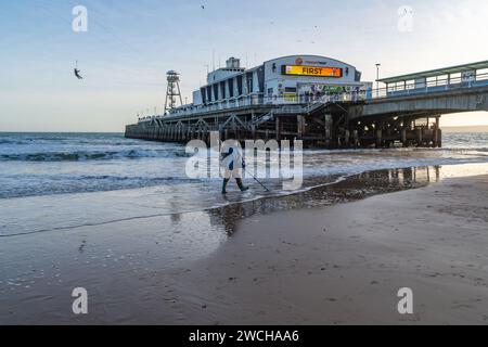 Bournemouth, UK - February 19th 2023: A man with a Metal Detector passing Bournemouth Pier with someone on a zip wire. Stock Photo