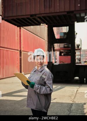 young asian female worker wearing safety helmet and working with container box at shipping yard Stock Photo