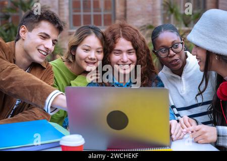 Group of smiling students, preparing for university exams, use a laptop outdoors Stock Photo