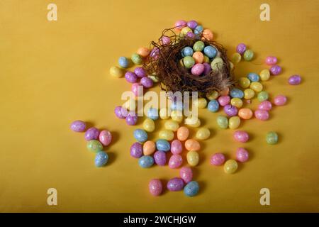 Tiny pastel colored Easter eggs spread against yellow surface and inside real bird's nest. Copy space to the left. Stock Photo