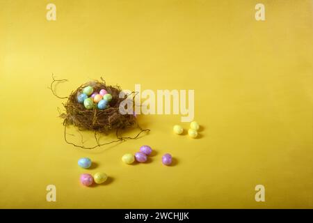 Tny bird's nest with small pastel colored Easter eggs. Horizontal photo against yellow background. Copy space to the right. Stock Photo