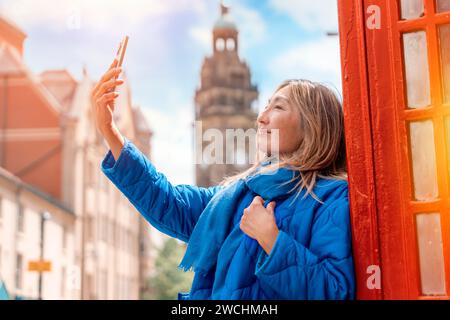 Outdoor portrait of asian woman using phone  against red phonebox visiting English city Stock Photo