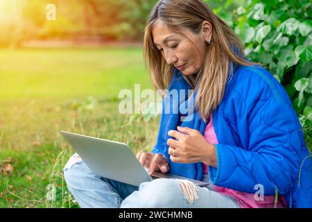 asian woman in blue jacket using laptop in public park  using internet everywhere Lifestyle concept Stock Photo