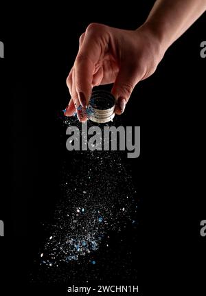 Female hand sprinkles glitter on dark background Stock Photo