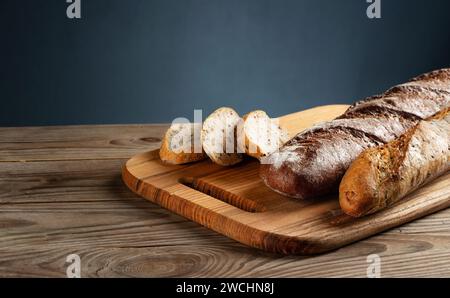 Freshly baked baguettes on a cutting board with chopped pieces on grey background. Stock Photo