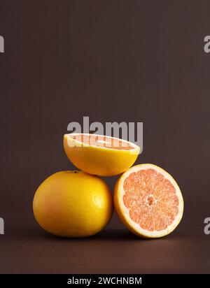 Whole and two halves of a grapefruit on a brown background. A source of vitamin C. Stock Photo