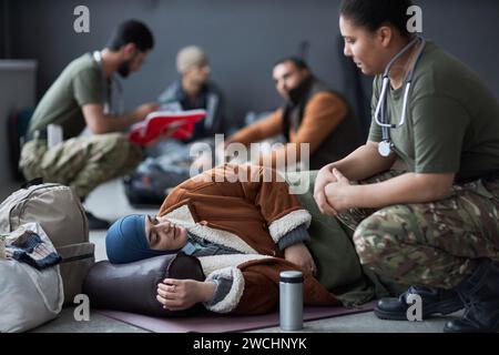 Portrait of Middle Eastern woman lying on floor at refugee shelter and talking to military doctor, copy space Stock Photo