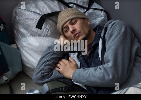 High angle portrait of Middle Eastern young man lying on floor at refugee shelter and looking away with sadness Stock Photo