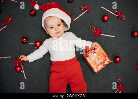 little baby boy in Santa's hat is lying among the festive Christmas candies, red balls and gift box Stock Photo