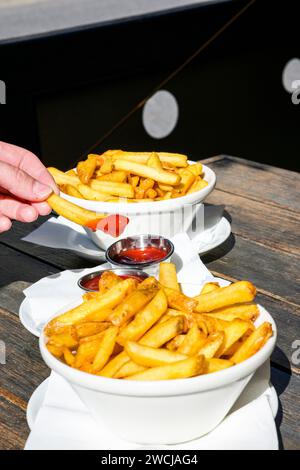 Fried fries with ketchup in a white bowl. A woman's hand holds a french fry dipped in ketchup. Stock Photo