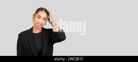 A professional young woman in a black blazer looks surprised, hand on head Stock Photo