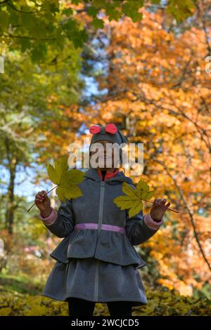 little smiling 7-year-old girl holds leaves from a tree in her hand, beautiful autumn blurred background. Stock Photo